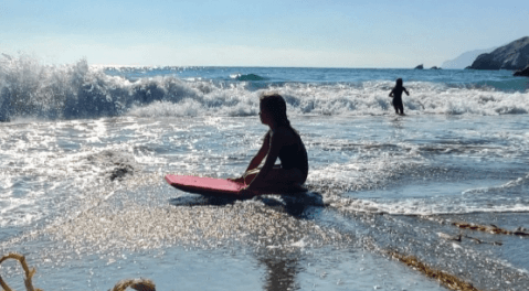 a child sitting on a boogie board at catalina shark harbor as waves come crashing in